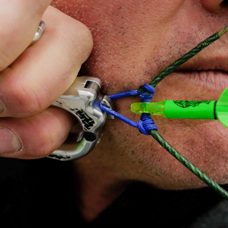 Close-up of John Dudley drawing back an arrow, focusing on the release and anchor point with a Nock On Archery branded arrow.
