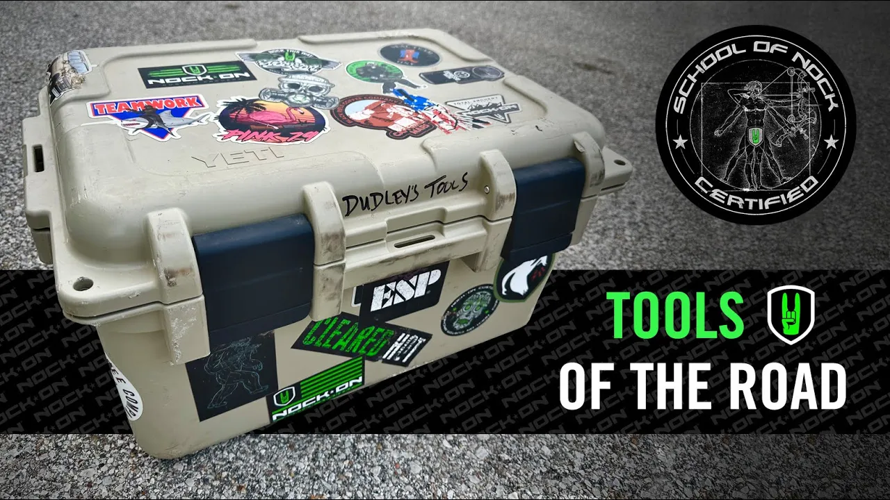 THE ULTIMATE ARCHERY BOX- Everything you need for archery repairs! 1 Custom tool kit covered with various stickers and labeled ‘Dudley’s Tools,’ placed on asphalt with the text ‘TOOLS OF THE ROAD’ and the ‘School of Nock Certified’ logo.