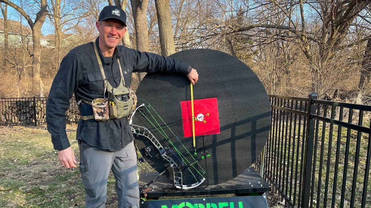 DON’T BE A DROP OUT! Things to consider about you arrow choice! 1 John Dudley standing beside an archery target with a compound bow, outdoors in a backyard setting, pointing to the target.