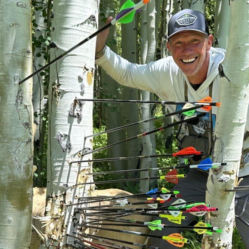 John Dudley standing by a tree with many arrows stuck in it.