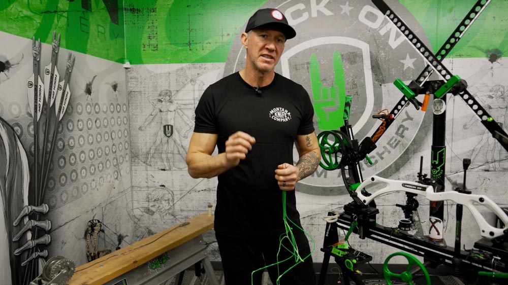 Bow Specs Not Matching Up? Post-String-Change Adjustments Made Easy 1 John Dudley discussing the importance of correct bow string alignment, with a compound bow and archery targets in the background.