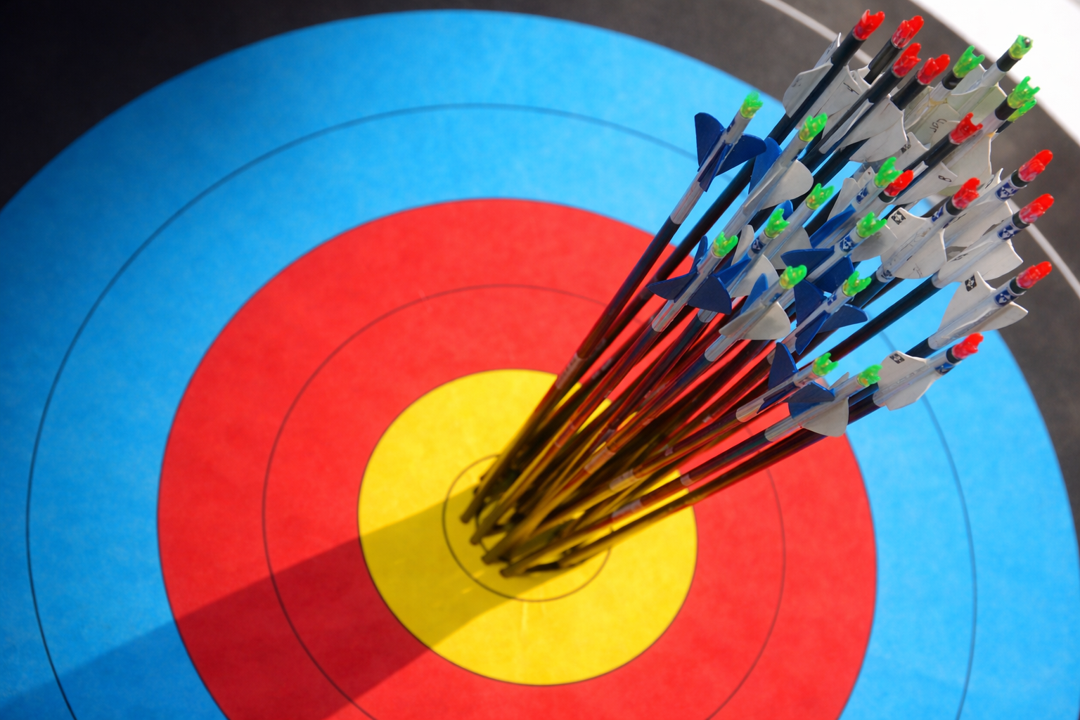 Close-up of arrows grouped tightly in the yellow bullseye of a blue, red, and yellow archery target.
