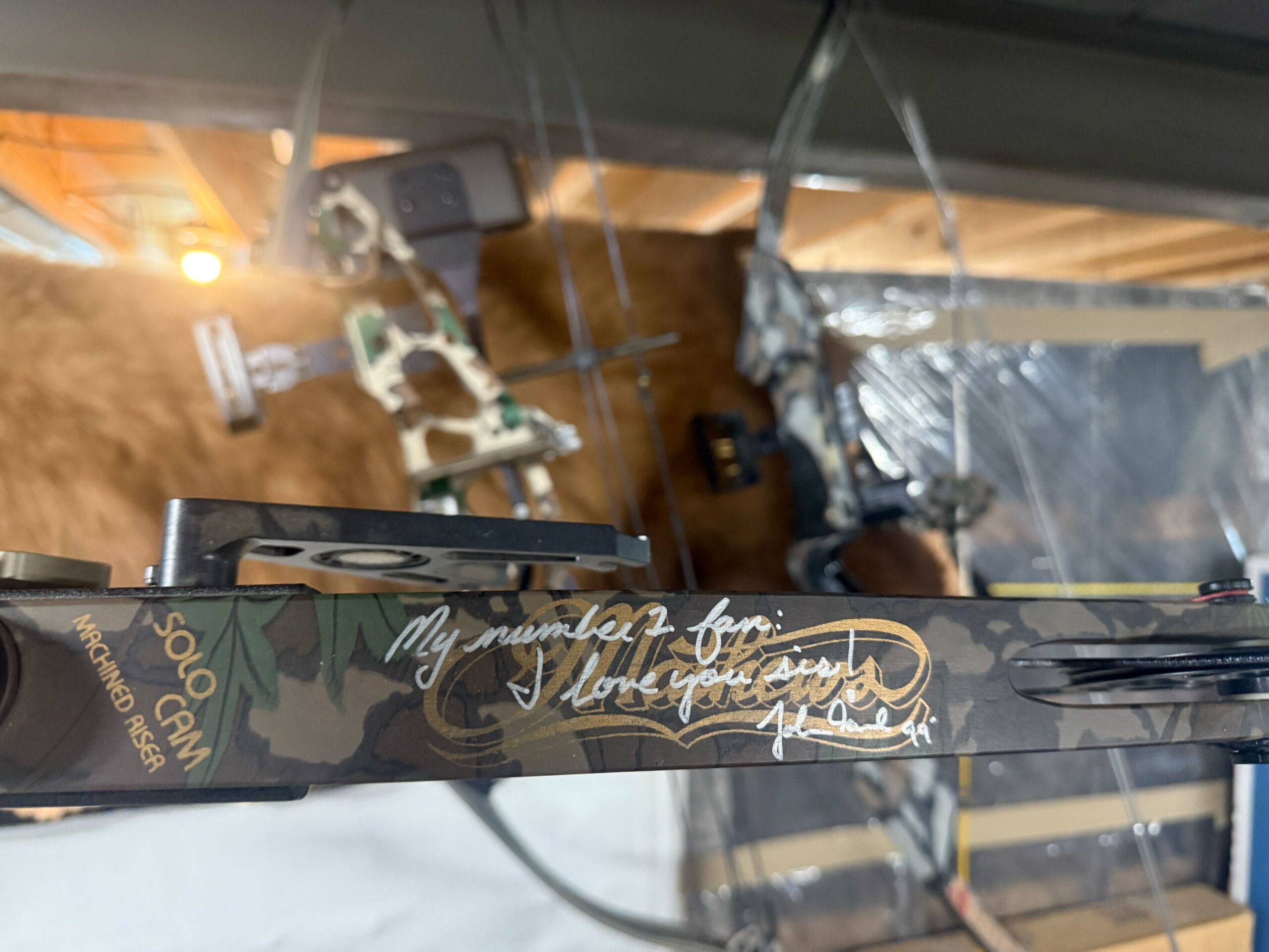 Signed Solo Cam compound bow with camo finish and handwritten dedication reading "My number 1 fan: I love you sis!" with artist signature.