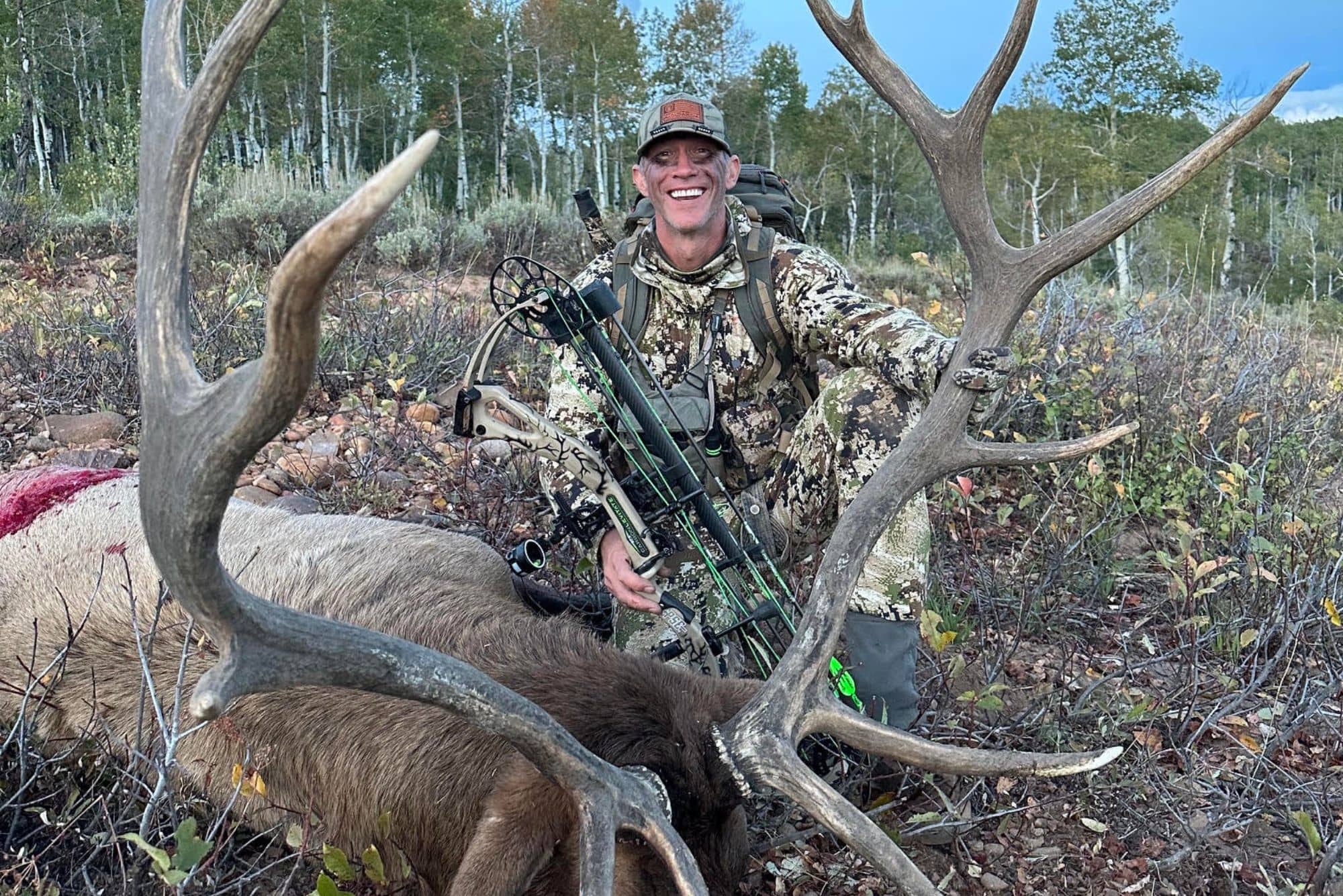 John holds his bow in one hand, and the large antlers of his latest elk tag in the other.