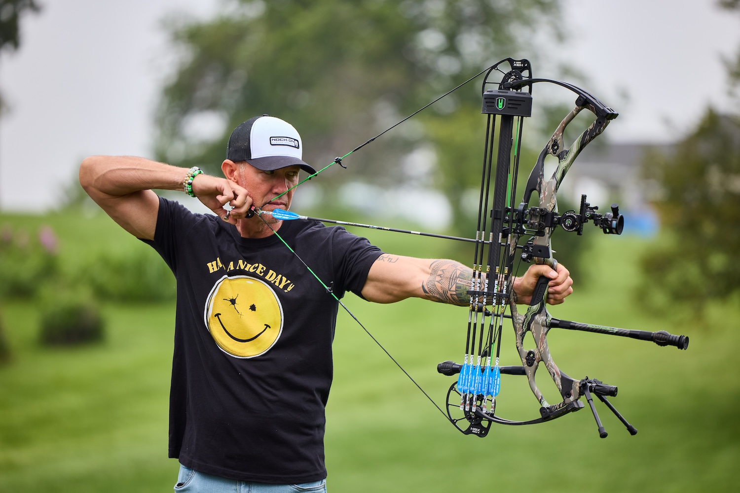 write alt text Archer at full draw with a camo compound bow outdoors.